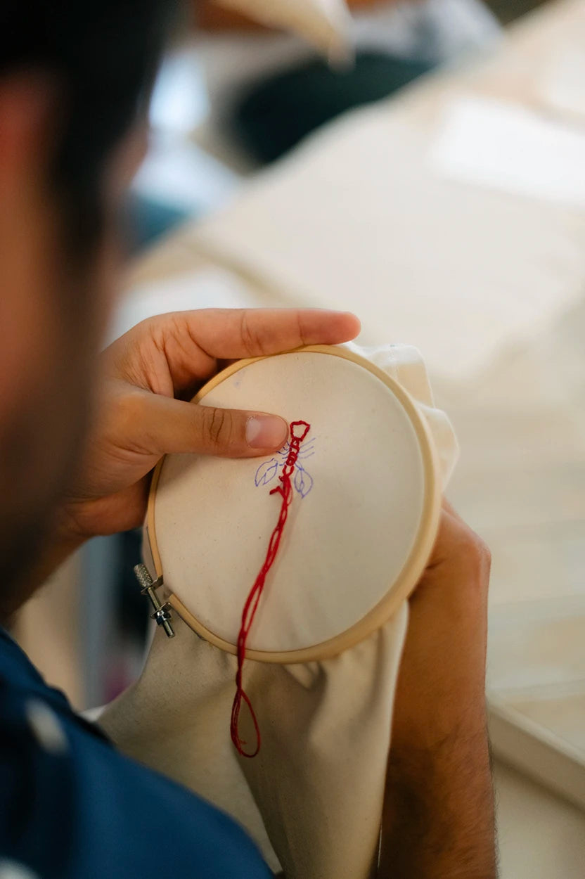 Primer plano de manos realizando bordado artístico sobre tela blanca en un taller de Jugo Club Textil.