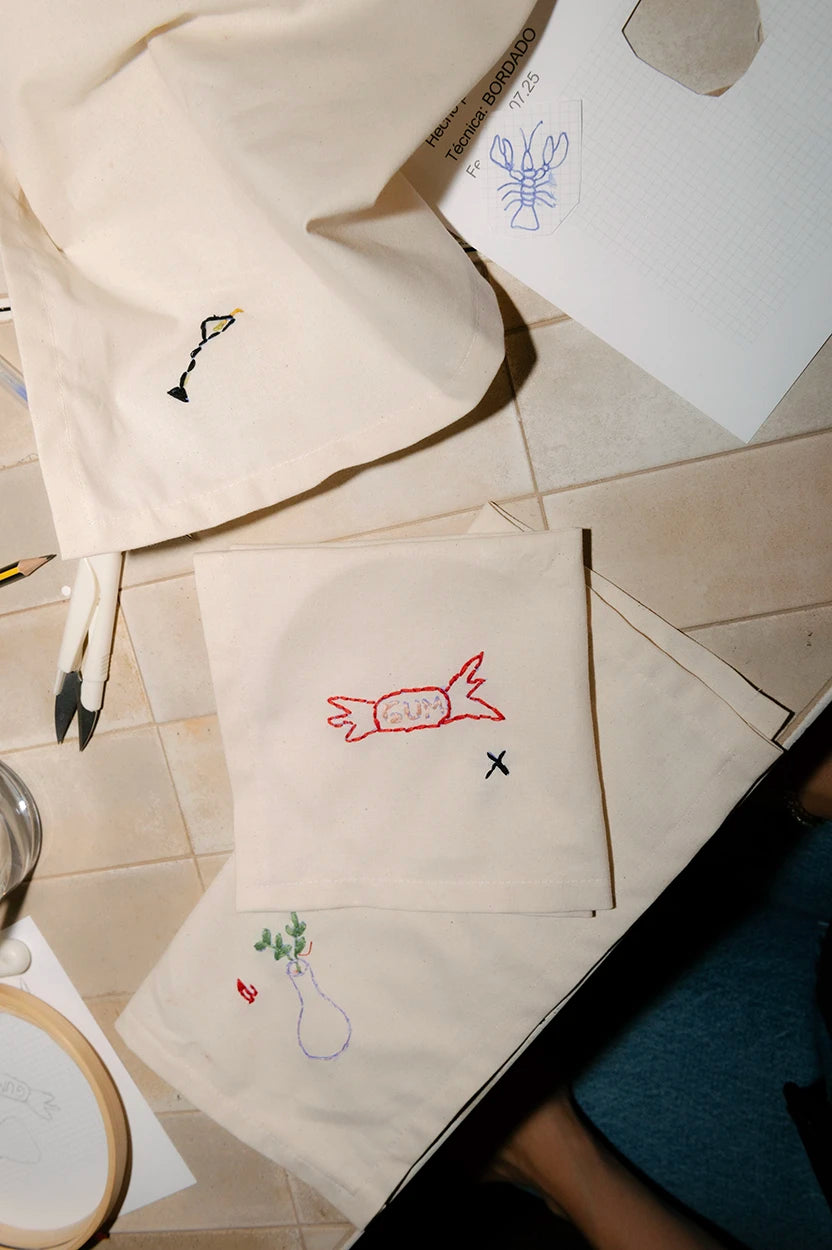 Diferentes diseños de bordado artístico hechos a mano sobre bolsas de tela, incluyendo un caramelo rojo y una copa, creados en Jugo Club Textil.