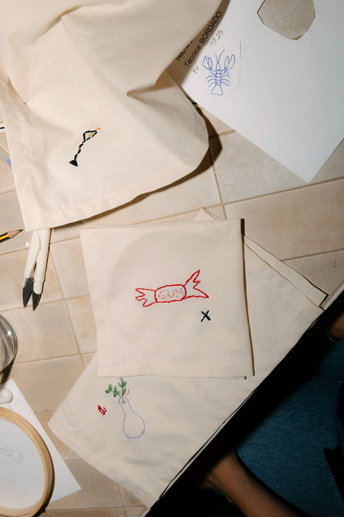 Diferentes diseños de bordado artístico hechos a mano sobre bolsas de tela, incluyendo un caramelo rojo y una copa, creados en Jugo Club Textil.