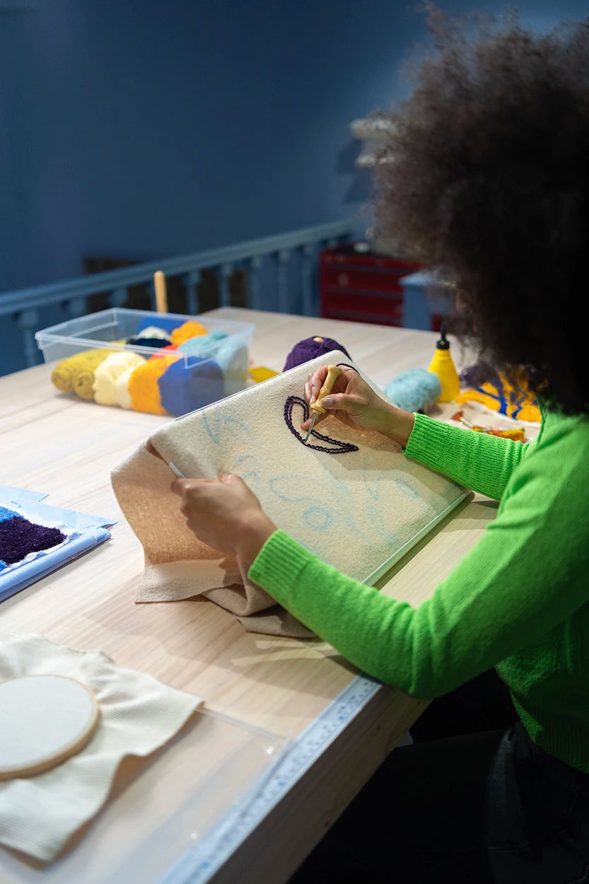 Participante de un taller de iniciación en Jugo aprendiendo la técnica de punch needle sobre un bastidor redondo con hilos de colores.