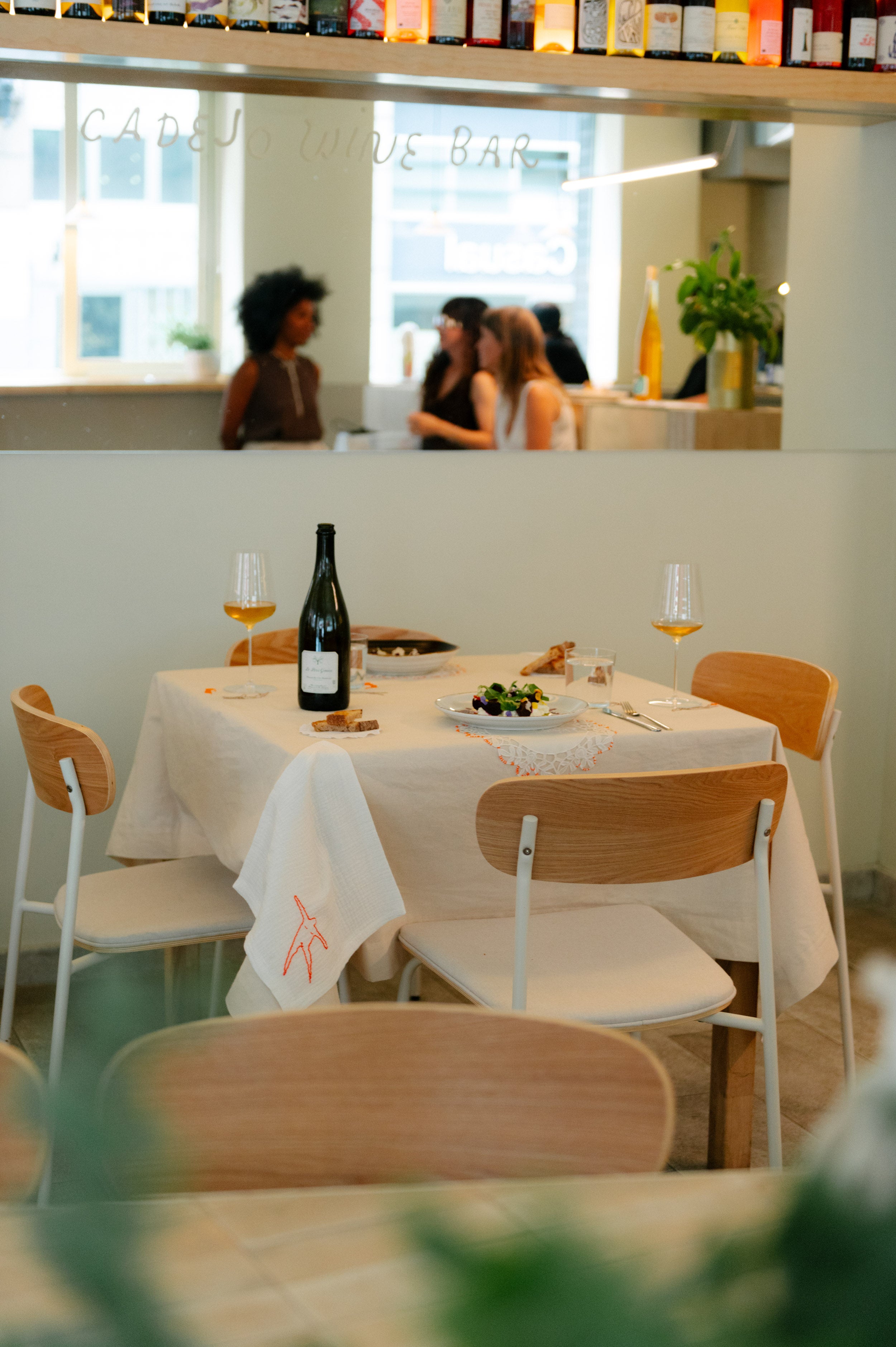 Mesa montada con mantel y servilletas bordadas de Jugo Project en un ambiente de restaurante moderno y luminoso