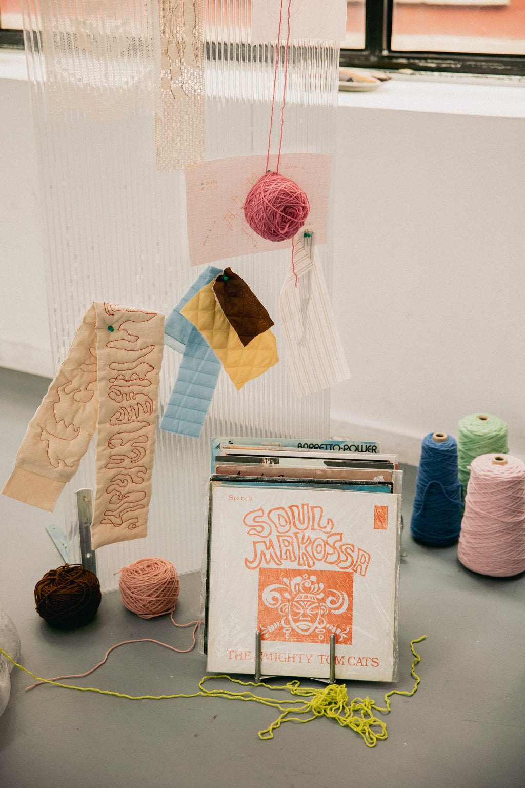 Bodegón artístico de Jugo Project con muestras de tejido tufting, ovillos de lana de colores y discos de vinilo en un taller luminoso.