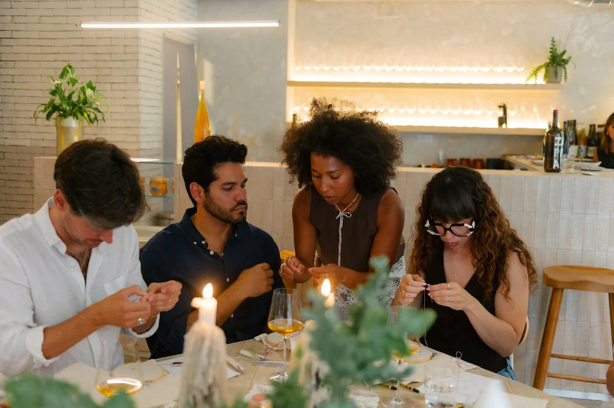 Cuatro personas concentradas trabajando en sus piezas artesanales durante un taller de Jugo Club Textil en un ambiente cálido con velas.